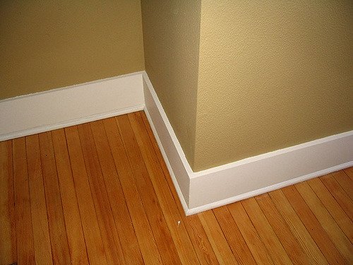 White baseboard wrapping an outside wall corner above hardwood flooring — trim carpentry