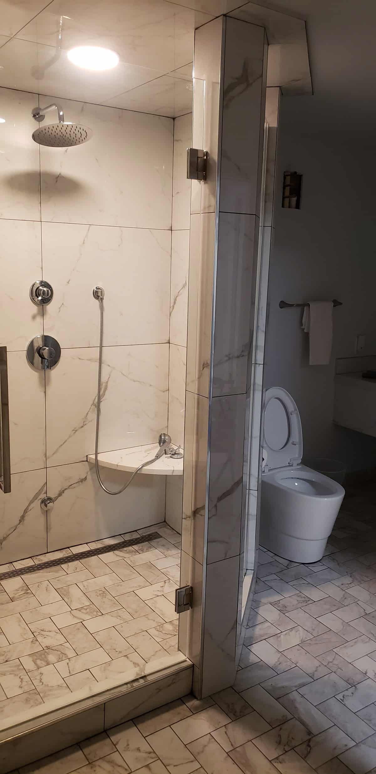 Finished luxury bathroom with Calacatta marble shower enclosure, rain head and chrome fixtures, separate wall-hung toilet, marble herringbone floor