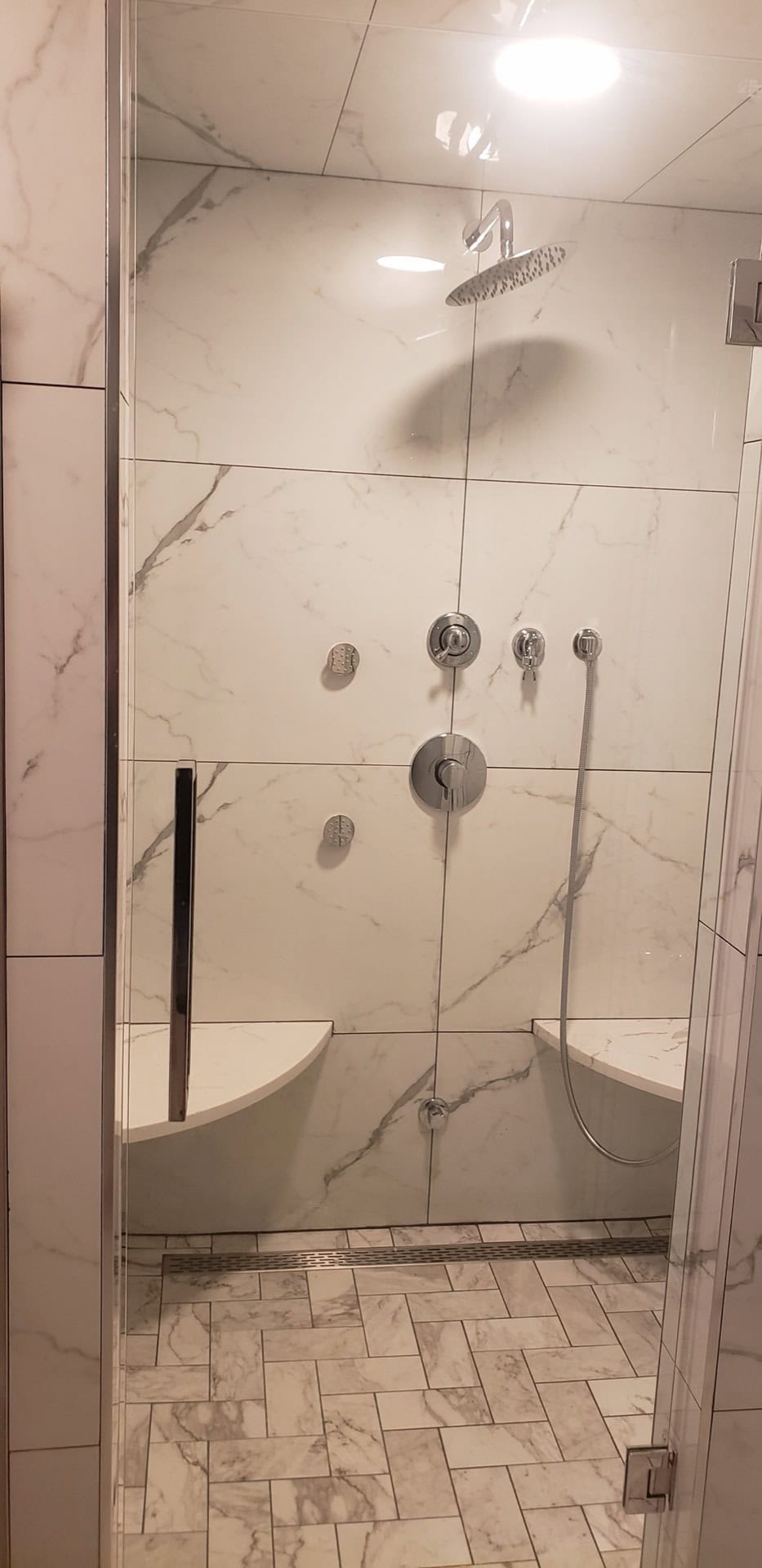 Finished luxury shower: Calacatta marble porcelain walls, chrome rain head and multi-jet fixtures, herringbone marble floor, built-in corner seats