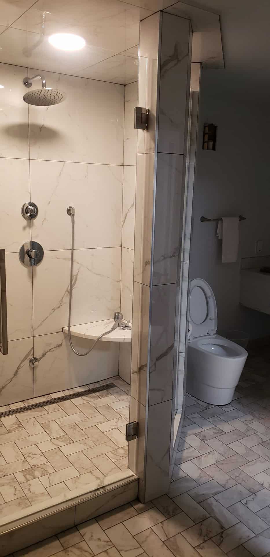 Finished luxury bathroom: Calacatta marble shower enclosure with rain head and chrome fixtures, separate wall-hung toilet, marble herringbone floor