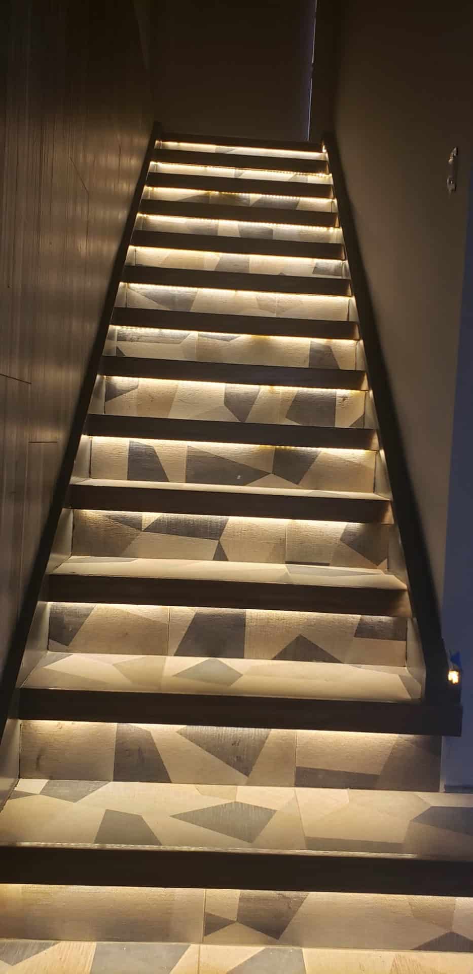 Custom LED-lit staircase with warm LED strips on each riser and geometric stone mosaic tile pattern on treads and floor