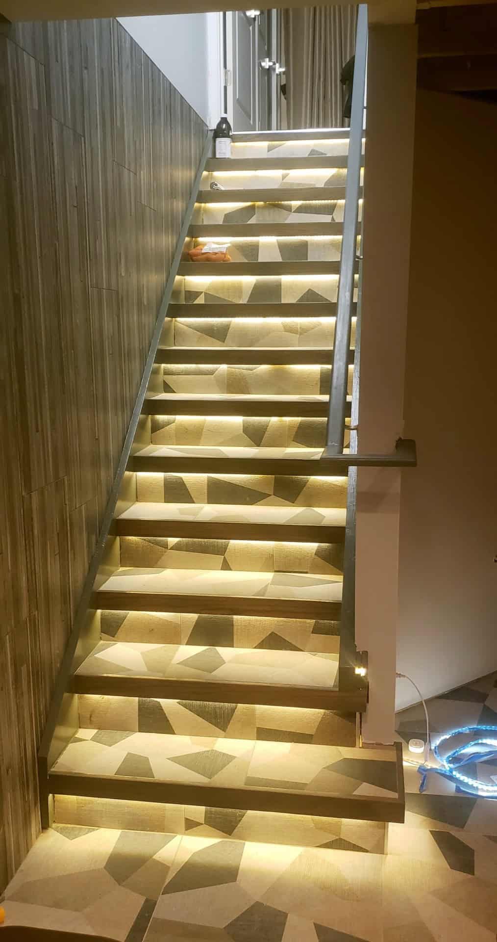 Wide shot of LED geometric mosaic staircase with warm LED risers and metal handrail