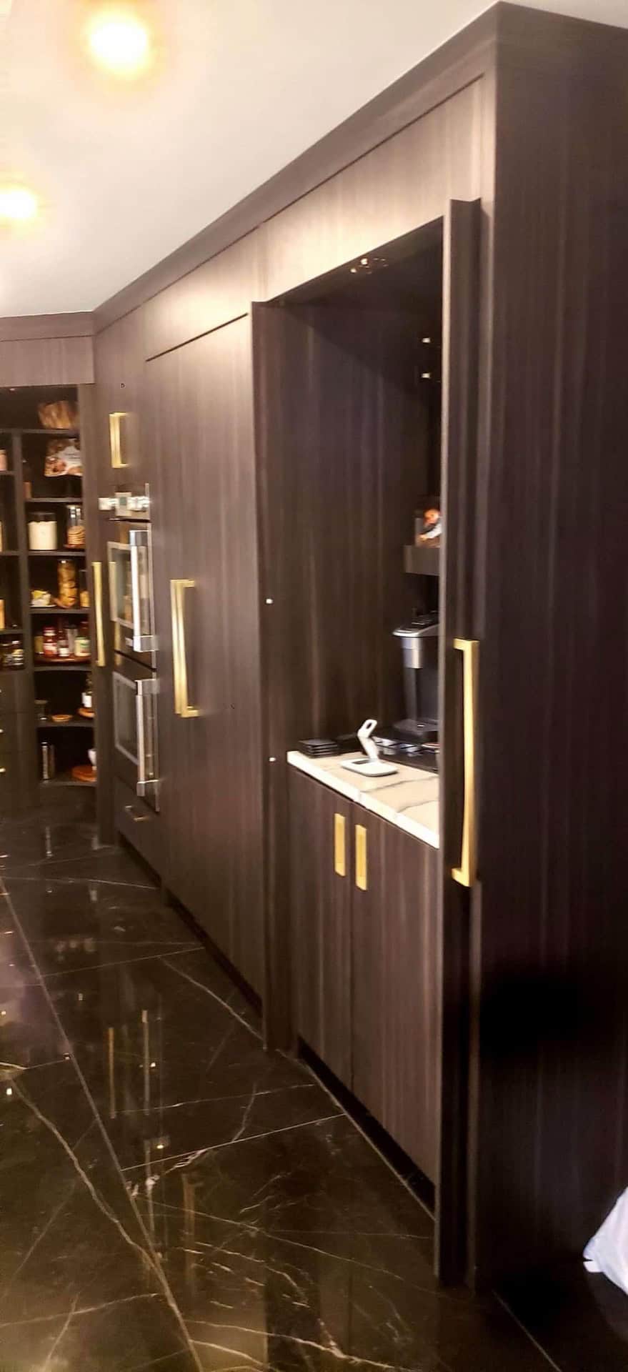 Dark wood-grain tall cabinetry with gold bar pulls and panel-ready refrigerator — kitchen remodeling