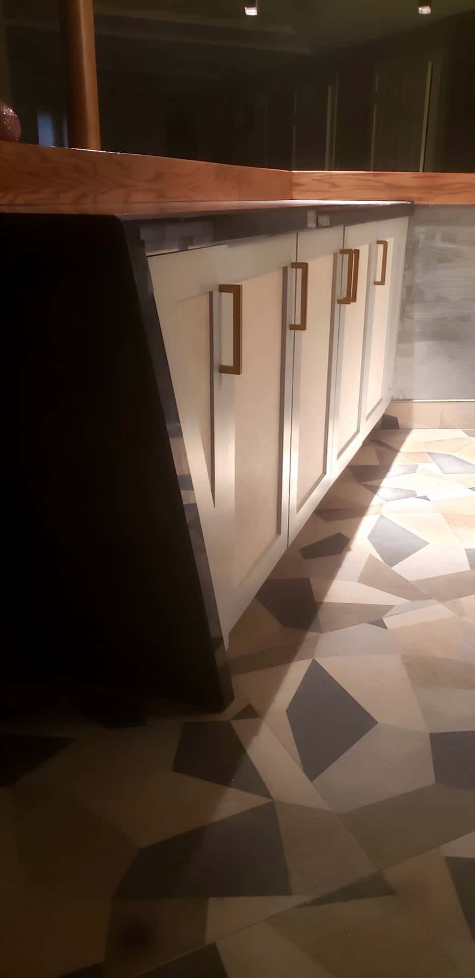 Basement bar corner detail: wood butcher block top, white cabinets with gold pulls, geometric mosaic floor