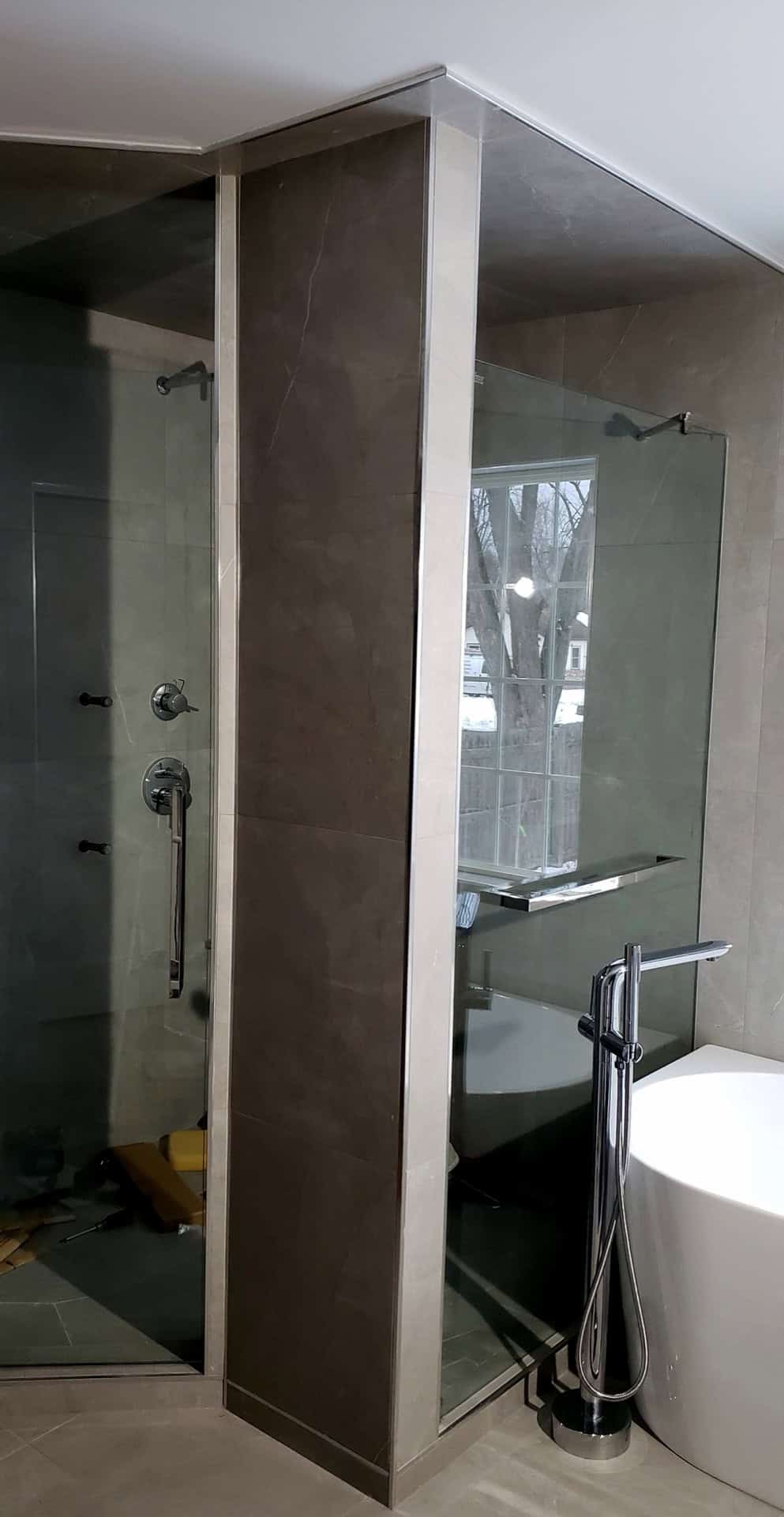 Bookmatched porcelain column with glass shower enclosure and freestanding tub — bathroom renovation