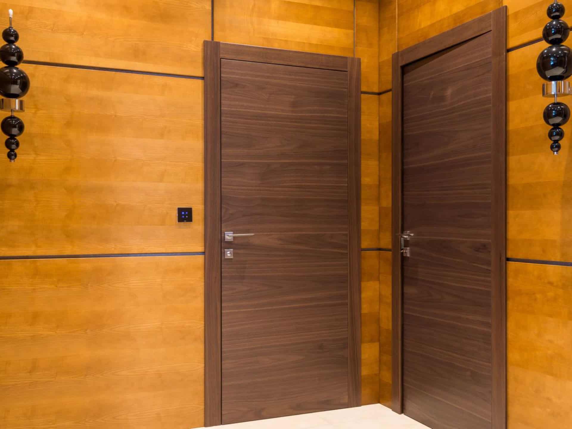 Two flush walnut interior doors with slim chrome lever handles set in a warm wood-panelled wall