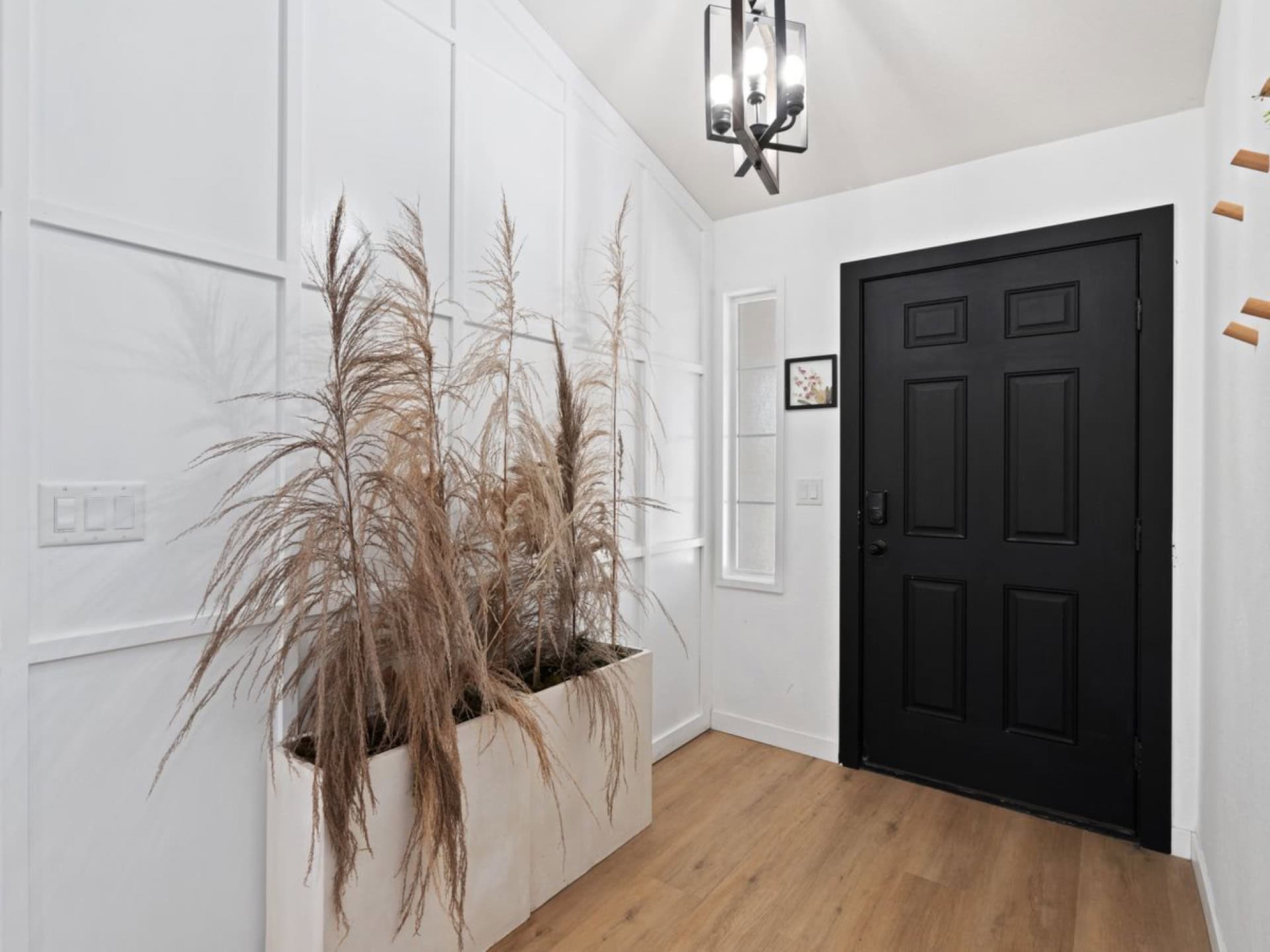 Entryway with a black six-panel front door, white board-and-batten panelled wall and light oak flooring